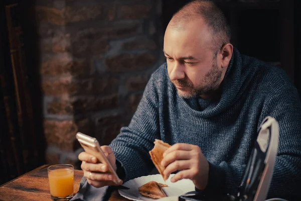 Homem Come Uma Sanduíche Olha Para Telefone Casa Homem Comum — Fotografia de Stock