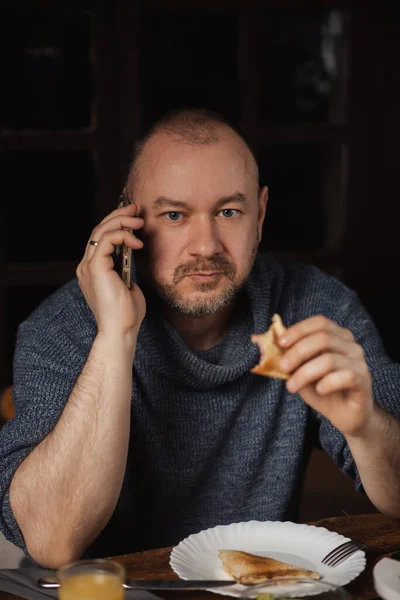 A man eats a sandwich and speaks on the phone. Ordinary middle-aged man. Eating with a phone in hand.