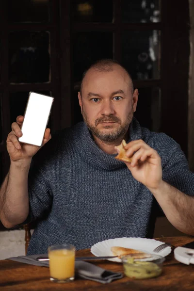 Homem Come Uma Sanduíche Tem Telefone Falso Nas Mãos Lugar — Fotografia de Stock