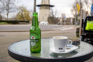 Rotterdam, Hollanda - 25 Mart 2023: Bir şişede Heineken birası ve bir yaz kafesinde bir fincan kahve.