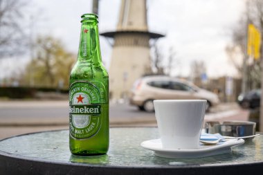 Rotterdam, Hollanda - 25 Mart 2023: Bir şişede Heineken birası ve bir yaz kafesinde bir fincan kahve.
