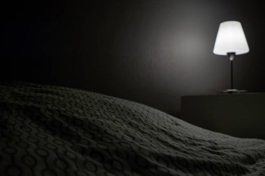 Bir komodin ve yanan bir lamba karanlık bir odada yatağın yanında duruyor. Otel numarası. Metin için yer.