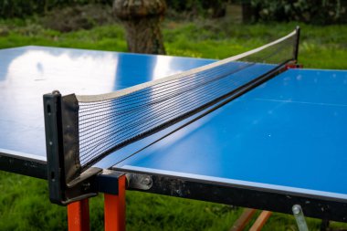 Yeşil çimlerin üzerinde pinpon masası. Küçük tenis oynamak için katlanan masa. Aktif boş zaman.