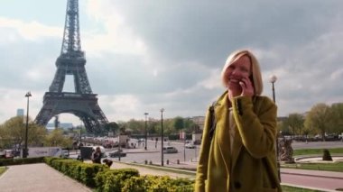Paris 'te Eyfel Kulesi' nin yakınında bir kadın telefonda konuşuyor. Güneşli bir günde, ceketli orta yaşlı bir kadın. turizm.