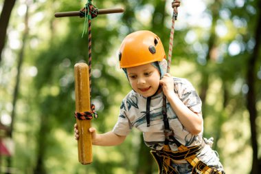 Dağ kenarındaki bir çocuk ve parmak arası terlik bir engelli parkurundan geçiyor. Bir çocuk için yazın aktif, sportif aktiviteler.