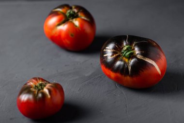 İnek kalbinin kırmızı-siyah domatesleri siyah arka planda çeşitlilik gösterir..