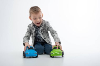 Genç bir çocuk beyaz arka planda çok renkli oyuncak arabalarla oynuyor. Çocuk eğlencesi, eğlence..