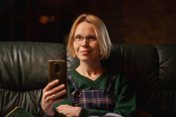 Жінка Окулярах Тримає Мобільний Телефон Руках Сидячи Дивані Жінка Середнього — стокове фото