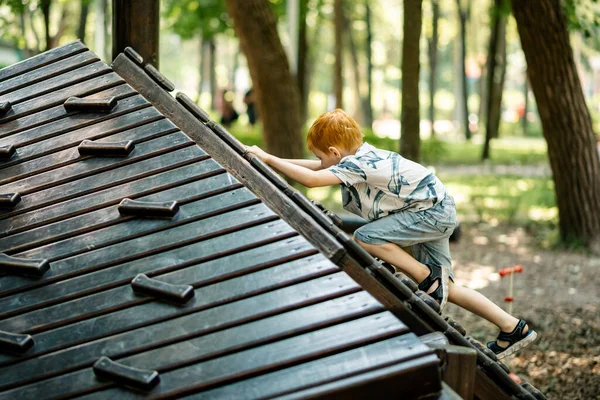 一个小男孩正在操场上爬木滑梯 积极的暑假 — 图库照片