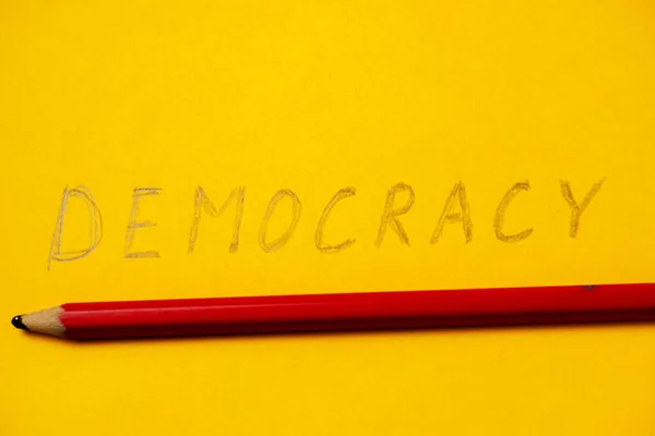 用铅笔写在黄色背景上的民主这个词 — 图库照片