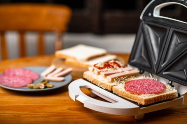 Sandviç makinesi ve sandviç yapma. Farklı malzemeler ahşap masada yan yana yatar..