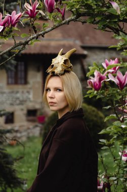 Kafasında hayvan kafatası olan ceketli bir kadının profili. Çiçekli manolya.