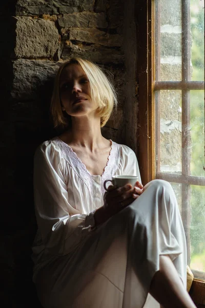 ウィンドウではパーティシャルルックの女性がコーヒーを飲む 白いシャツを着た中年女性 悲しいな — ストック写真