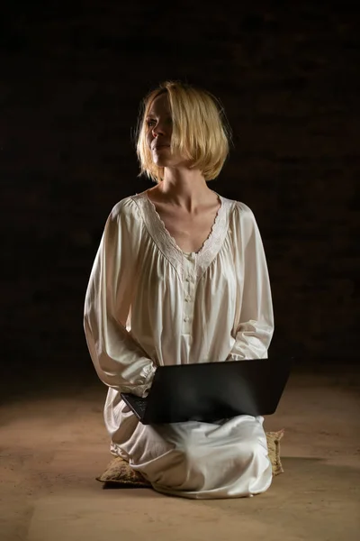 stock image Woman and laptop in an empty dark room. Middle age woman in a white shirt.