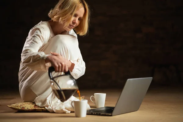 Женщина Наливает Кофе Сидя Перед Ноутбуком Пустая Комната Темный Фон — стоковое фото