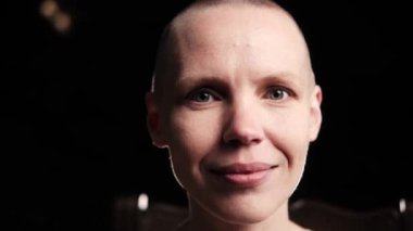 Siyah arka planda gülümseyen kel bir kadın..