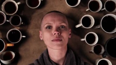 Bir sürü kahveden sonra uykusuz kadın. Bir sürü kahveyle çevrili kel bir kadının portresi. Son teslim tarihi, fazla mesai konsepti.