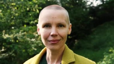 Yeşil paltolu kel, orta yaşlı bir kadın yeşil bir arka planda. Özgürlük, zafer, kemoterapi konsepti.