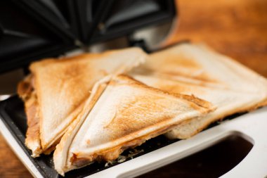 Tahta bir arka planda sandviç makinesinde yeni yapılmış tost sandviçler. Peynirli üç köşeli sandviç..