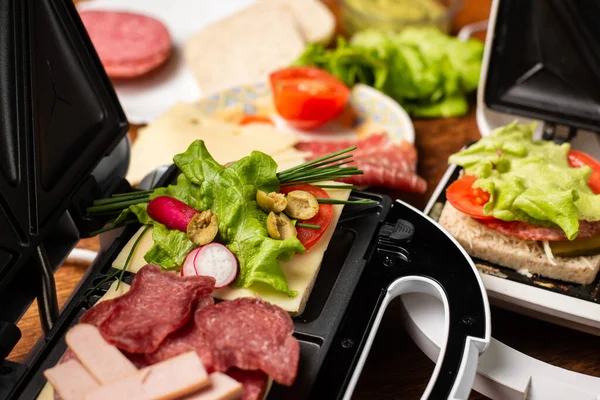 Stock image Different types of sandwiches in a sandwich maker on a wooden background with different ingredients. Place for text.