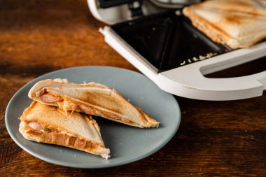 Ahşap bir arka planda bir tabakta sandviç yapan birinden yeni yapılmış tost sandviçler. Peynirli üç köşeli sandviç..