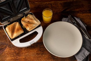 Kızarmış sandviçler, boş bir tabak ve ahşap arka planda bir bardak portakal suyu. Hafif sabah kahvaltısı, atıştırmalık.