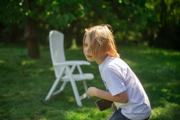 一个长发的小男孩在阳光灿烂的日子里在绿色的草地上玩耍 — 图库照片