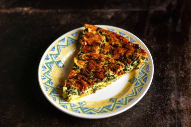 Koyu arkaplanda bir tabakta taze yapılmış ıspanaklı ve peynirli turta. Vejetaryen turtası.