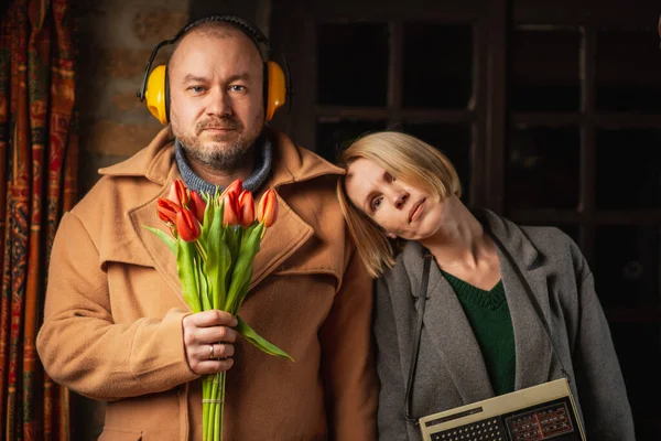 カップルのばかばかしい面白い写真 チューリップの花束を持つ男と暗い部屋にレトロなラジオを持つ女性 — ストック写真