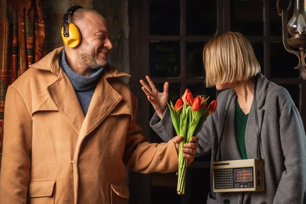 レトロなラジオを持つ女性にチューリップの花束を与えるノイズからヘッドフォンで男の面白い写真 — ストック写真