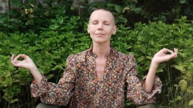 Bir kadın dışarıda meditasyon yapıyor. Nane çalılarının önünde kel, orta yaşlı bir kadın. Huzur bulmak, akıl sağlığı..
