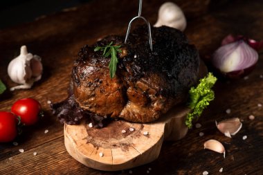 Ahşap tezgahta pişmiş bir parça et ve çiğ sebze. Baharatlı fırında pişirilmiş domuz ya da sığır eti..