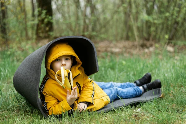 Молодий Хлопчик Лежить Туристичному Килимку Лісі Їсть Банан — стокове фото