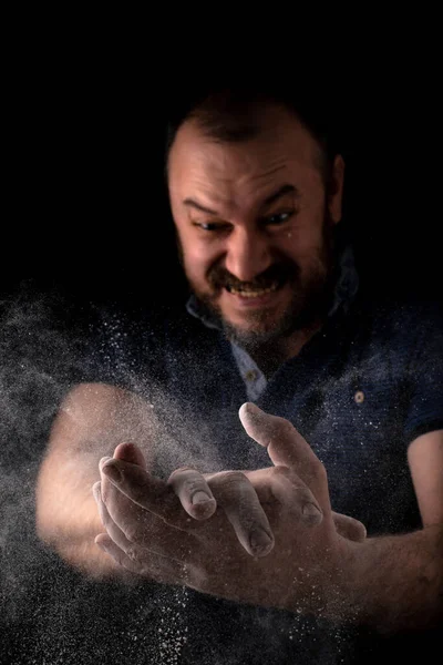 The man claps his hands emotionally with anguish. A cloud of flour scatters from male hands on a black background. Cooking concept.
