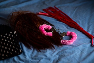 Kırmızı kürklü, kırbaçlı ve peruklu kelepçeler. Yataktaki aşk oyunları için aygıtlar.