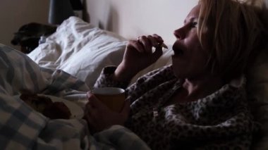 Kadın yatakta yemek yiyor. Orta yaşlı kadın kahve içer ve kurabiye yer..