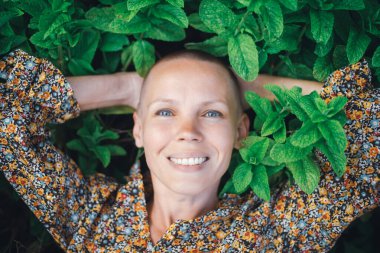 Kadın nane yapraklarının içinde yatıyor. Orta yaşlı kel bir kadın gülümsüyor ve kameraya bakıyor. Aromaterapi, sağlık konsepti.