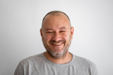 Sıradan görünümlü, traşsız bir adam gülüyor ve gri arka plandaki kameraya bakıyor. Kırklı yaşlarda bir adam.