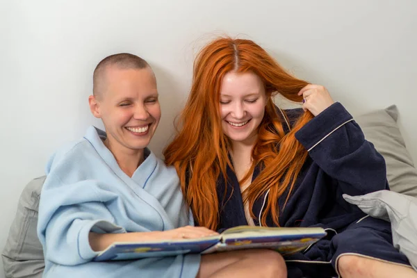 Joyful interaction in a pair of lesbians while reading a book. Joy and pleasure from joint leisure. A woman with short hair and a girl with long red hair.