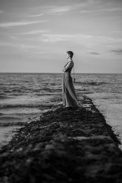 A woman with a short haircut stands on the ocean and smiles. Relaxation, time to be alone with yourself. Loneliness, sadness. Black and white image.