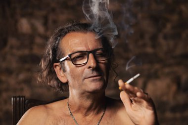 Yaklaşık 60 yaşında, Sırp uyruklu, uzun saçlı ve gözlüklü yaşlı bir adam, koyu bir arkaplanda düşünceli bir şekilde sigara içiyor. Sanatçı, yaratıcı kişi. Mutlu yüz..