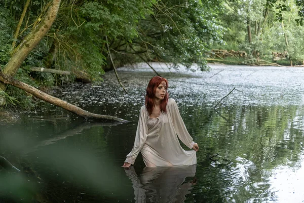 stock image A young teenage girl in a white dress stands in a lake against a background of green foliage. day Ivan bathed.