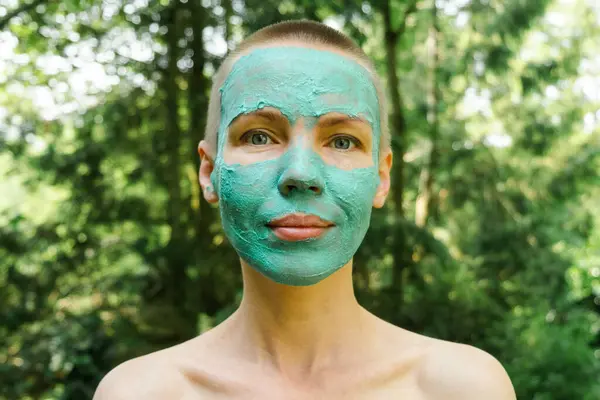 A middle-aged woman in a cosmetic mask lies against the background of a green forest. Woman with short hair.