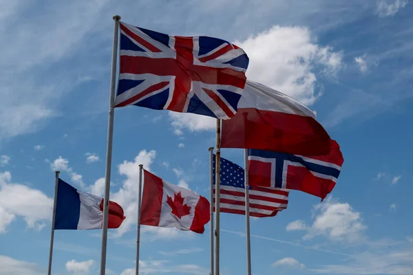 Many different flags fluttering in the wind against the sky. Great Britain Canada England France