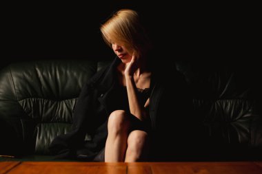 Bir kadın düşünceli bir şekilde karanlık bir odada bir koltuğa oturur, düşünme noktasında, ağır düşünceler içinde.