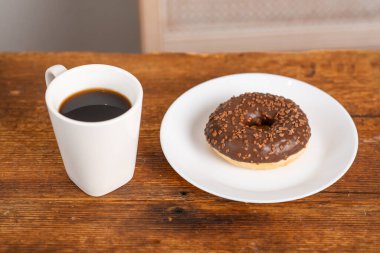 Beyaz tabakta çikolatalı çörek ve tahta arka planda bir fincan kahve. Sabah kahvaltısı