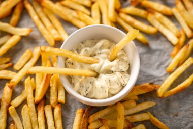 İçinde otlar ve patates kızartması olan beyaz sos, pişmiş altın patates kızartmasının arka planına yapışmış.