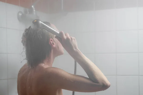 A woman at heart. Woman washing her hair in the shower in the mist of hot water