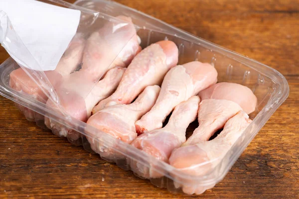 Fresh chicken legs in a plastic box on a wooden background