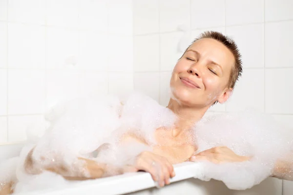 A woman with a short haircut delights in her bubble bath, her face reflecting pure bliss and relaxation